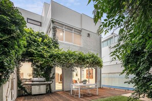 Ein modernes Gebäude mit einer Terrassenfläche, die einen Grill, einen Tisch mit Stühlen und einen Blick ins Innere bietet.