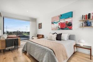 Ein modernes Schlafzimmer mit einem großen Bett, Blick durch eine Schiebetür, einem Bücherregal und einem Bild an der Wand.
