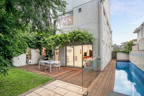 Ein modernes Haus mit Pool, einer Terrasse mit Tisch und Stühlen sowie eine Glastür, die zu einem Wohnbereich führt.