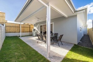Eine überdachte Terrasse mit Tisch und Stühlen, einem Deckenventilator und einem Holzzaun im Hintergrund.