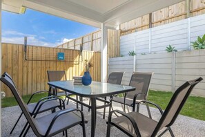 Eine Terrasse im Freien mit Tisch und Stühlen, einem Holzzaun und einer weißen Mauer.