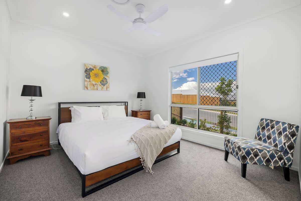 Una camera da letto con un letto, due comodini, una sedia, una ventola a soffitto, una finestra con vista e un quadro al muro.