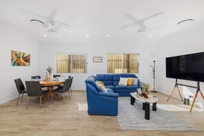 Ein modernes Wohnzimmer mit einem blauen Sofa, einem Esstisch, Stühlen und einem Fernseher auf einem Stativ.