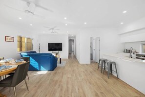 Ein moderner Wohnraum mit Essbereich, einem blauen Sofa, einem Fernseher und einer Küchenzeile mit Barhocker.