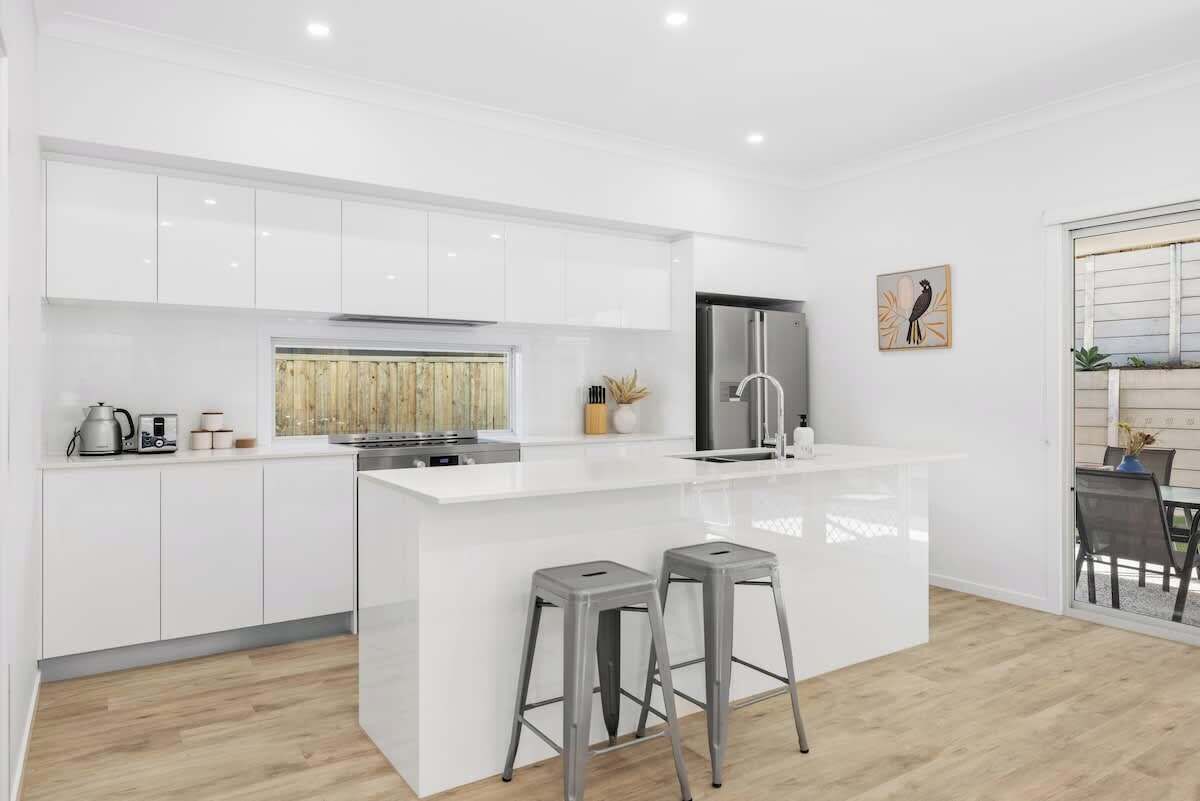 Une cuisine moderne avec des meubles blancs, un réfrigérateur en acier inoxydable et deux tabourets de bar.