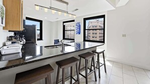 A modern kitchen with a large island, bar stools, and a view of buildings through large windows. - 2 BR Iconic Detroit High-Rise Loft (Detroit)