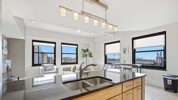 A modern kitchen with a large island, double sinks, and large windows offering city views. - Urban Loft Living in Downtown Detroit & Gym (Detroit)