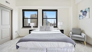 A hotel room with a large bed, two windows, a chair, and a painting on the wall. - Urban Loft Living in Downtown Detroit & Gym (Detroit)