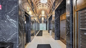 A marble-lined hallway with an ornate ceiling, elevators, and a black carpet. - Urban Loft Living in Downtown Detroit & Gym (Detroit)