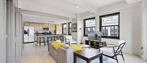 A modern kitchen with a central island, a dining area with a table and chairs, and a living area with a sofa and a TV.