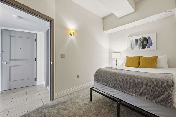 A bedroom with a bed, a bench, a wall-mounted light, and a door. - Urban Loft Living in Downtown Detroit, City View (Detroit)