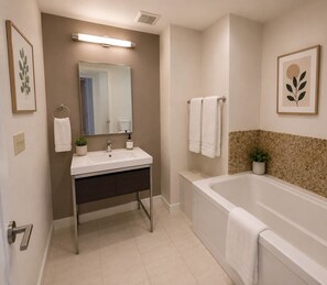 Un baño moderno con lavamanos, espejo y bañera blancos.