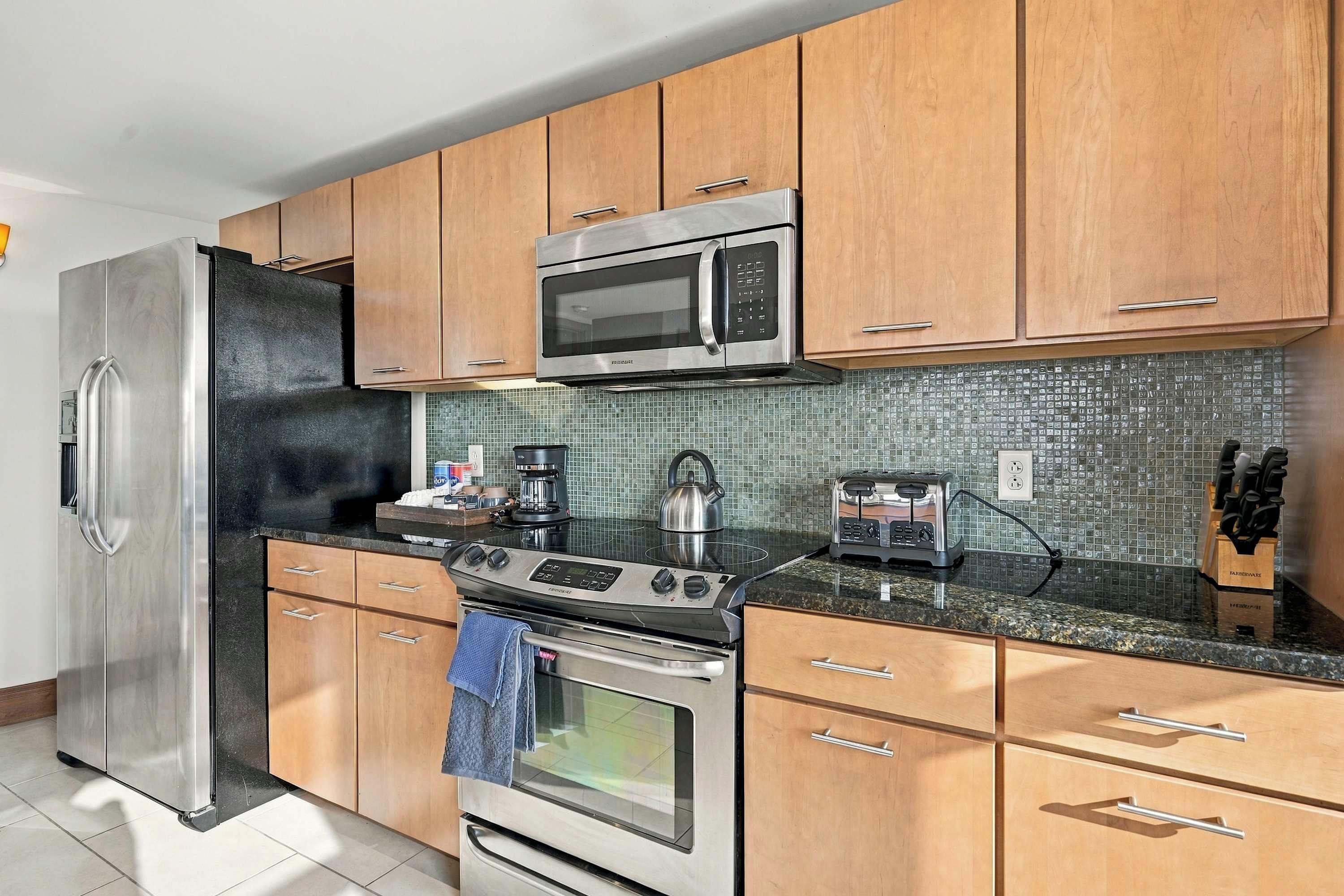 A modern kitchen with stainless steel appliances, wooden cabinets, a tiled backsplash, and a granite countertop.