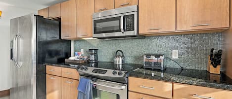 A modern kitchen with stainless steel appliances, wooden cabinets, a tiled backsplash, and a granite countertop.