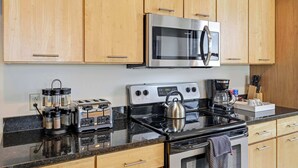 A modern kitchen with wooden cabinets, a stainless steel microwave, a gas stove, a coffee maker, and a toaster. - Urban Loft Living in Downtown Detroit & Gym (Detroit)