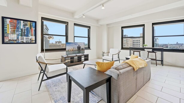 A modern living room with a sofa, chairs, a TV, and a dining area with a table and chairs. - Urban Loft Living in Downtown Detroit & Gym (Detroit)