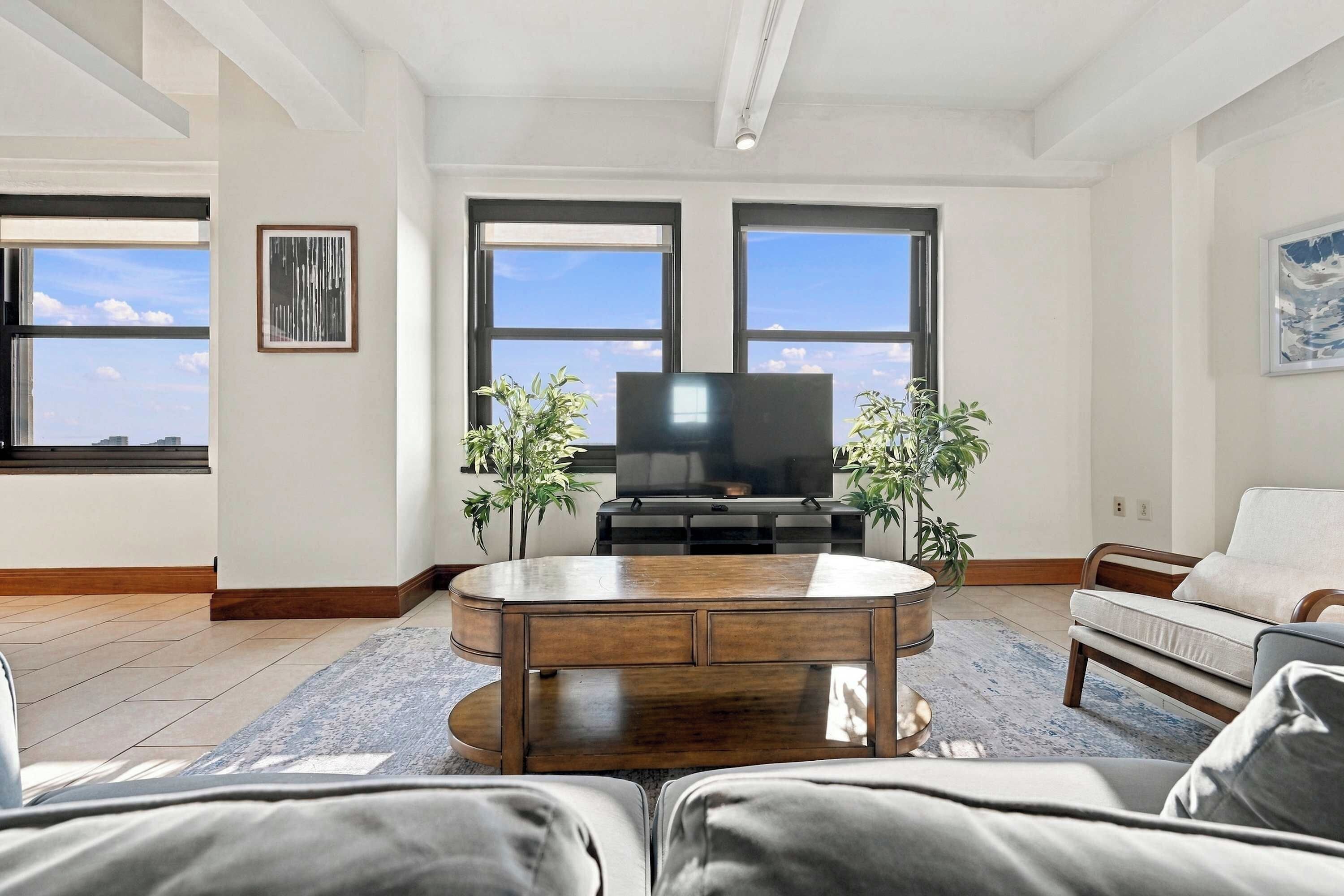 Una sala de estar con una televisión de pantalla plana, dos plantas en macetas, una mesa de centro de madera y un sofá.