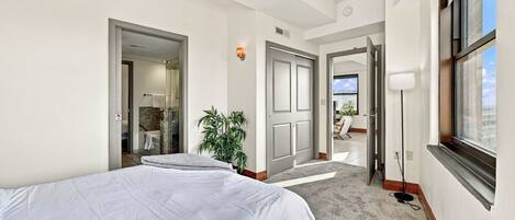 Een hotelkamer met een bed, een plant, een badkamer en uitzicht op buiten.