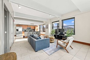 A modern living room with a sofa, a TV, and a dining area with a kitchen in the background. - Modern Loft Living in Downtown Detroit w City View (Detroit)