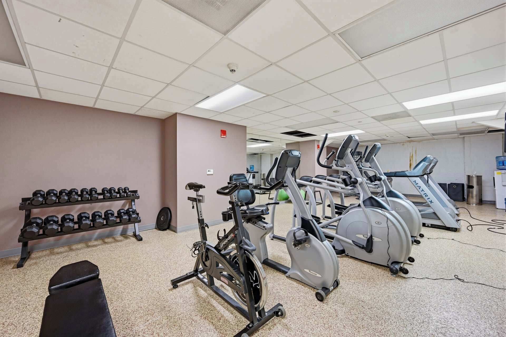 A gym with exercise equipment including dumbbells, a stationary bike, and treadmills.