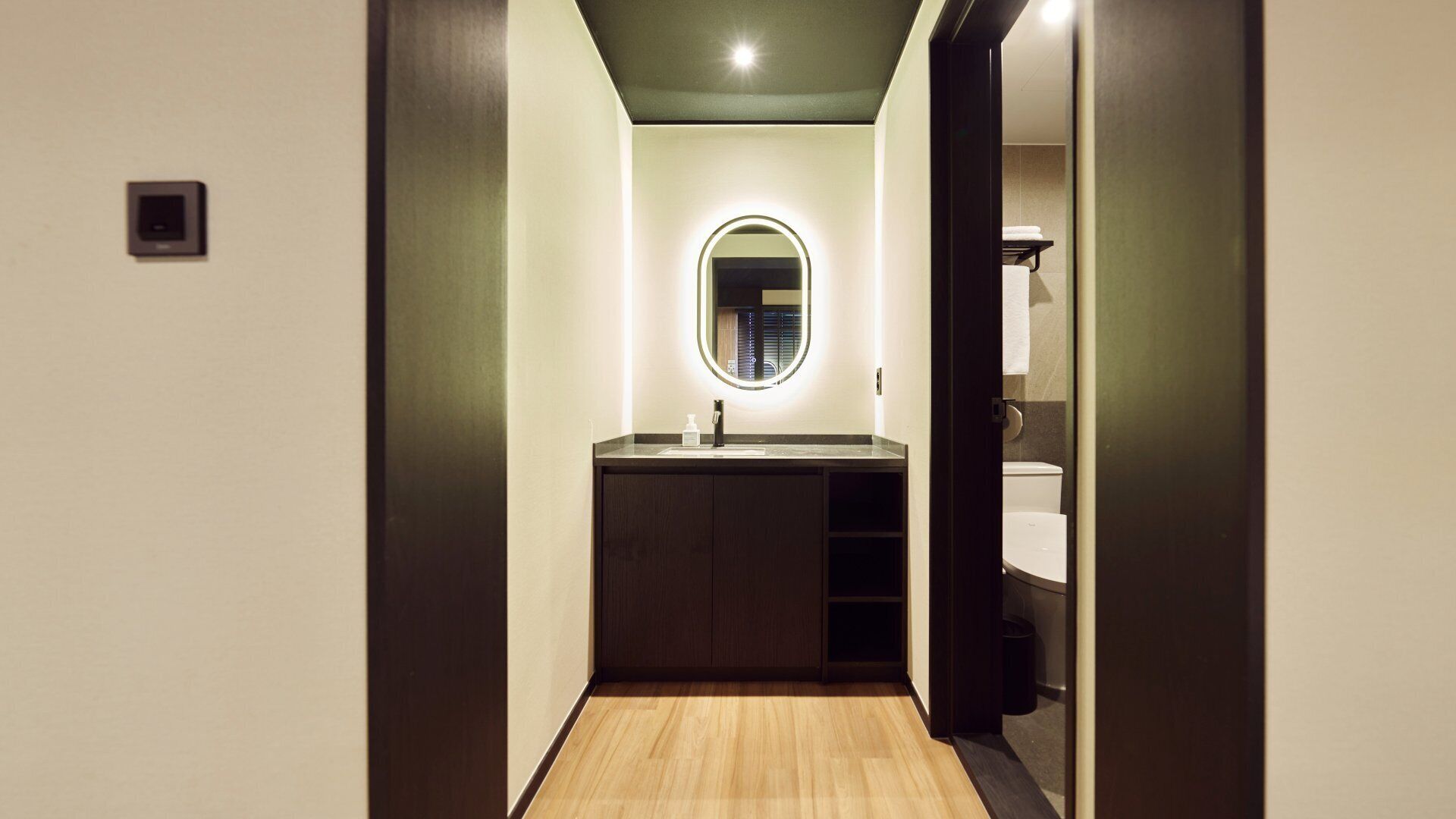 Passadís estret amb terra de fusta que condueix a un bany amb un lavabo i un mirall.