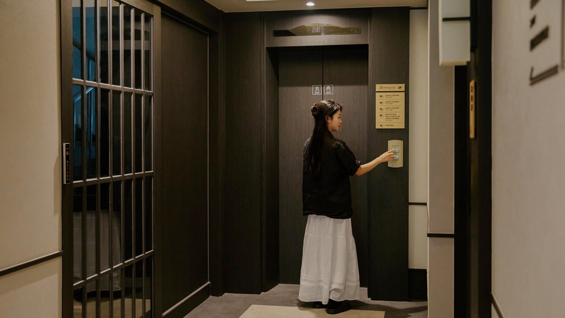 Una persona de pie en un pasillo con una puerta que indica '2F', señalando el segundo piso.