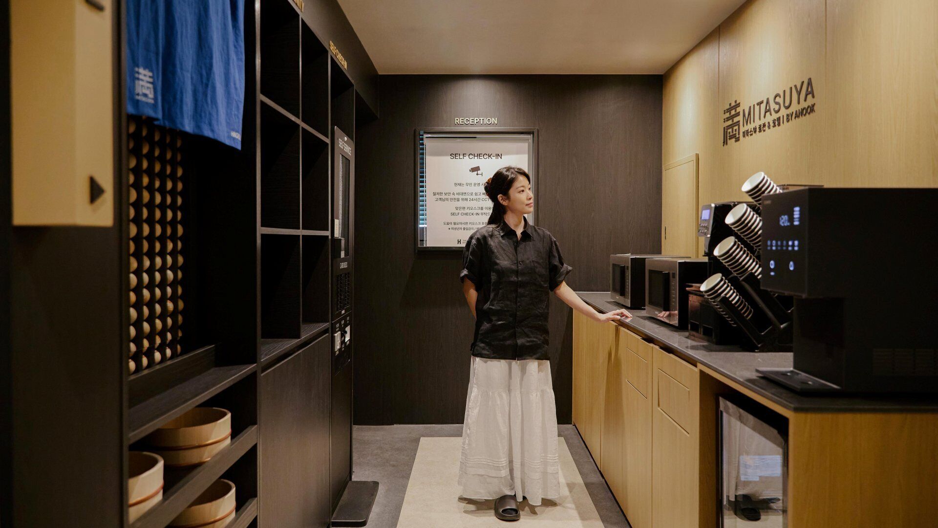 Un espace d’accueil d’hôtel comprenant un terminal d’enregistrement automatisé, des meubles en bois et un comptoir de réception.