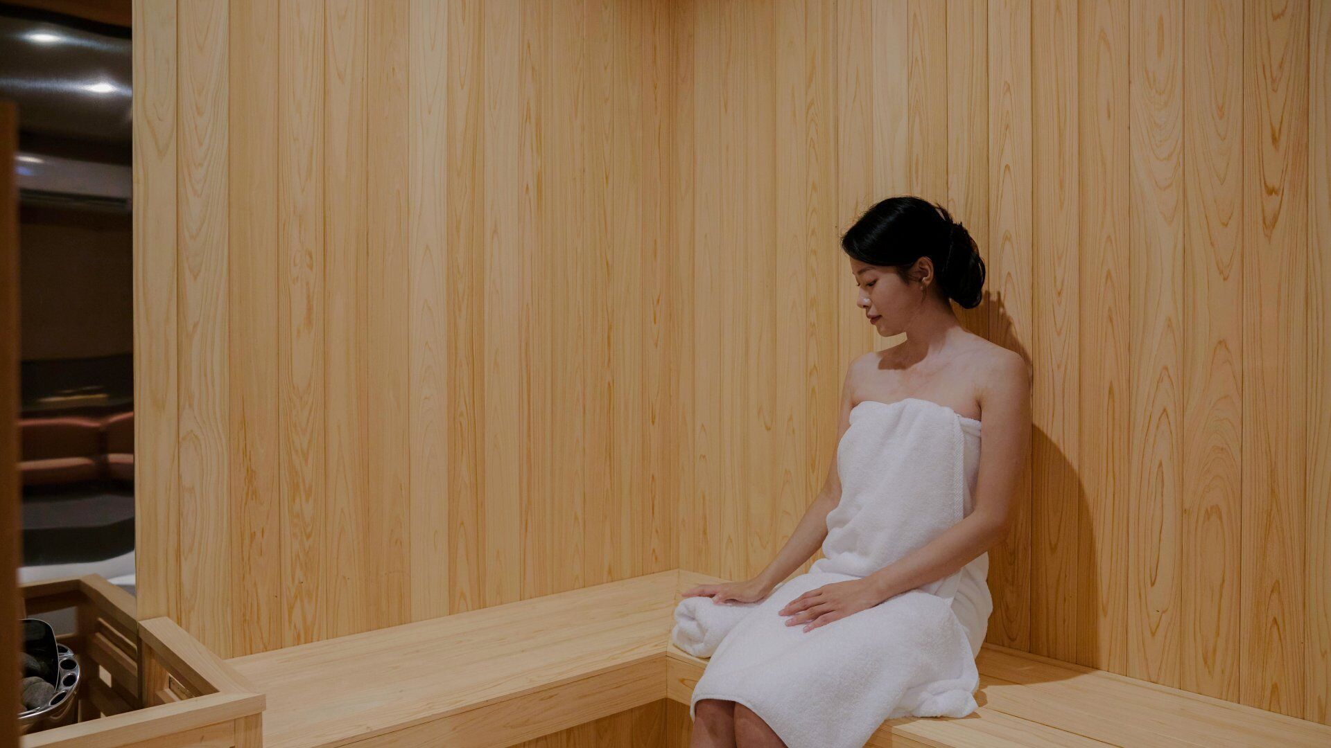Una persona sentada en una sauna de madera con un banco.