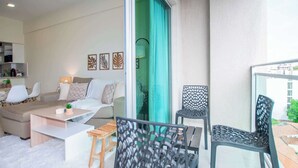 Een moderne woonkamer met een bank, salontafel en stoelen, een balkon met uitzicht, en een eethoek met een tafel en stoelen.