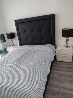 Un lit bien fait, avec une couvre-lit à rayures, une tête de lit noire recouverte de tissu et deux tables de chevet avec des lampes.