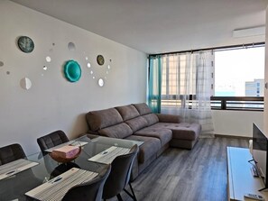 Un salon moderne avec une table à manger en verre, un canapé marron et un téléviseur posé sur un meuble.