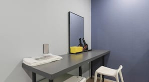 Una habitación con un escritorio gris, una silla blanca, un espejo y una caja amarilla.