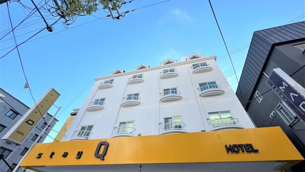 Un edificio de hotel con un llamativo letrero amarillo que dice 'Stay Q HOTEL' y un balcón en el segundo piso.