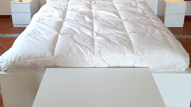 A neatly made bed with white bedding and two bedside tables with lamps.