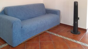 A room with a blue sofa and a standing fan.