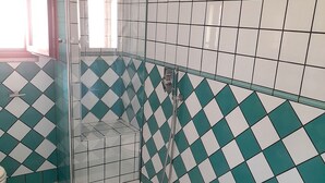 A bathroom with a glass shower enclosure, a white sink, and a tiled floor with a checkered pattern.