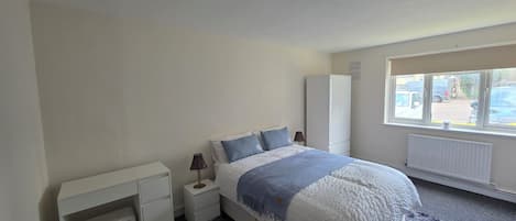 Un dormitorio con cama, mesita de noche, escritorio, armario y ventana con vistas al exterior.