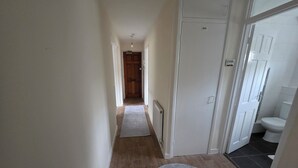 A narrow hallway with a wooden floor, a white door, and a visible bathroom with a toilet and sink. - Modern 2BDR Flat Near Stratford and Central London (Greater London)