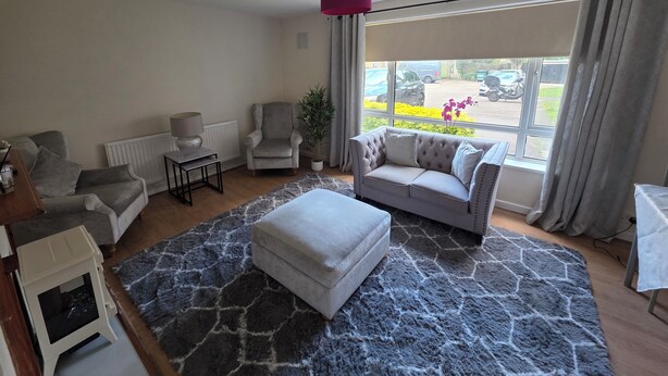 A living room with a grey sofa, a white ottoman, a small table with a lamp, a chair, and a potted plant. - Modern 2BDR Flat Near Stratford and Central London (Greater London)