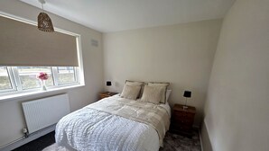 A bedroom with a bed, two bedside tables, a window with a view, a radiator, and a hanging light fixture. - Modern 2BDR Flat Near Stratford and Central London (Greater London)