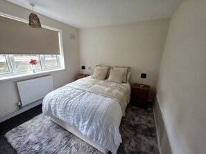 Een slaapkamer met een bed, twee nachtkastjes, een raam met uitzicht, een radiator en een hanglamp.