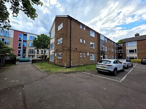 Ein mehrstöckiges Wohngebäude mit Parkplatz vor der Fassade.