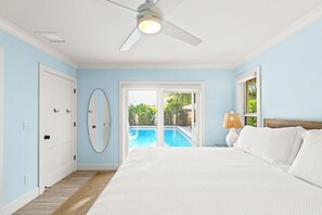 Ein Schlafzimmer mit Bett, Deckenventilator, Tür und Spiegel, mit Blick auf einen Swimmingpool.