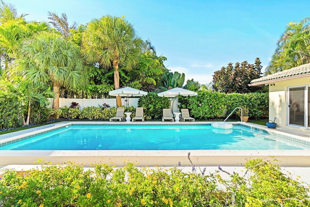 A swimming pool with lounge chairs and umbrellas, surrounded by lush greenery.