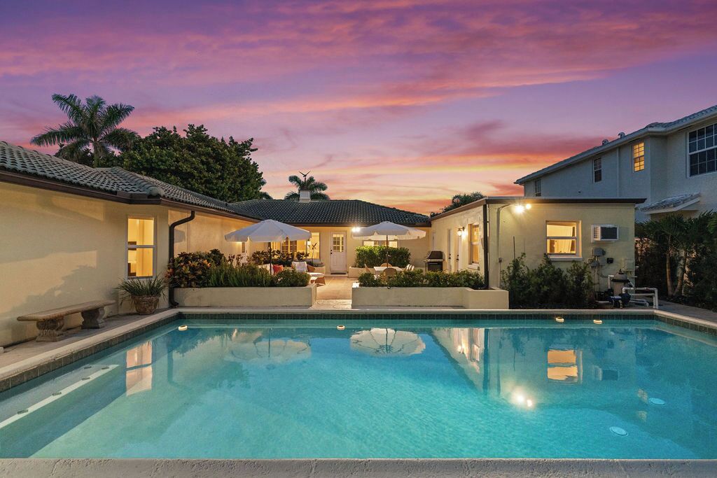 A swimming pool with a sunset sky, a patio area with umbrellas, and a house with a tiled roof.