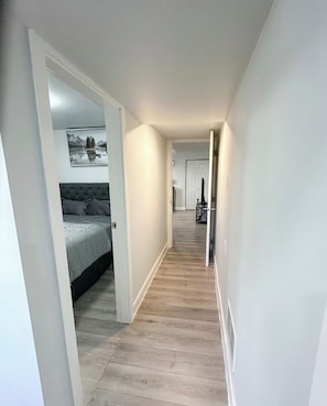 A narrow hallway with a bed on the left, a door at the end, and a staircase leading to another room. - Newly renovated private basement Suite - central hub (Vancouver)