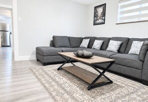 A modern living room with a grey sectional sofa, a wooden coffee table, and a patterned rug. - Newly renovated private basement Suite - central hub (Vancouver)