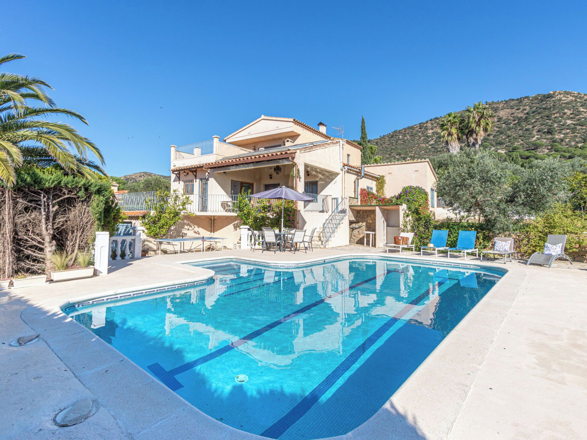 A poolside area with a pool, lounge chairs, and a building with a balcony.