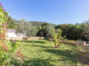 A garden with various plants and trees, a stone wall, and a clear blue sky. - Mestral by Interhome (Palau Savardera)