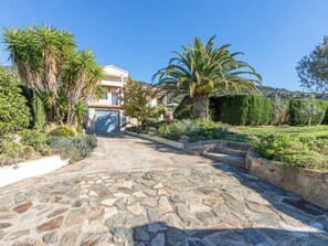 A stone pathway leading to a house with a blue door, surrounded by various plants and a clear blue sky. - Mestral by Interhome (Palau Savardera)